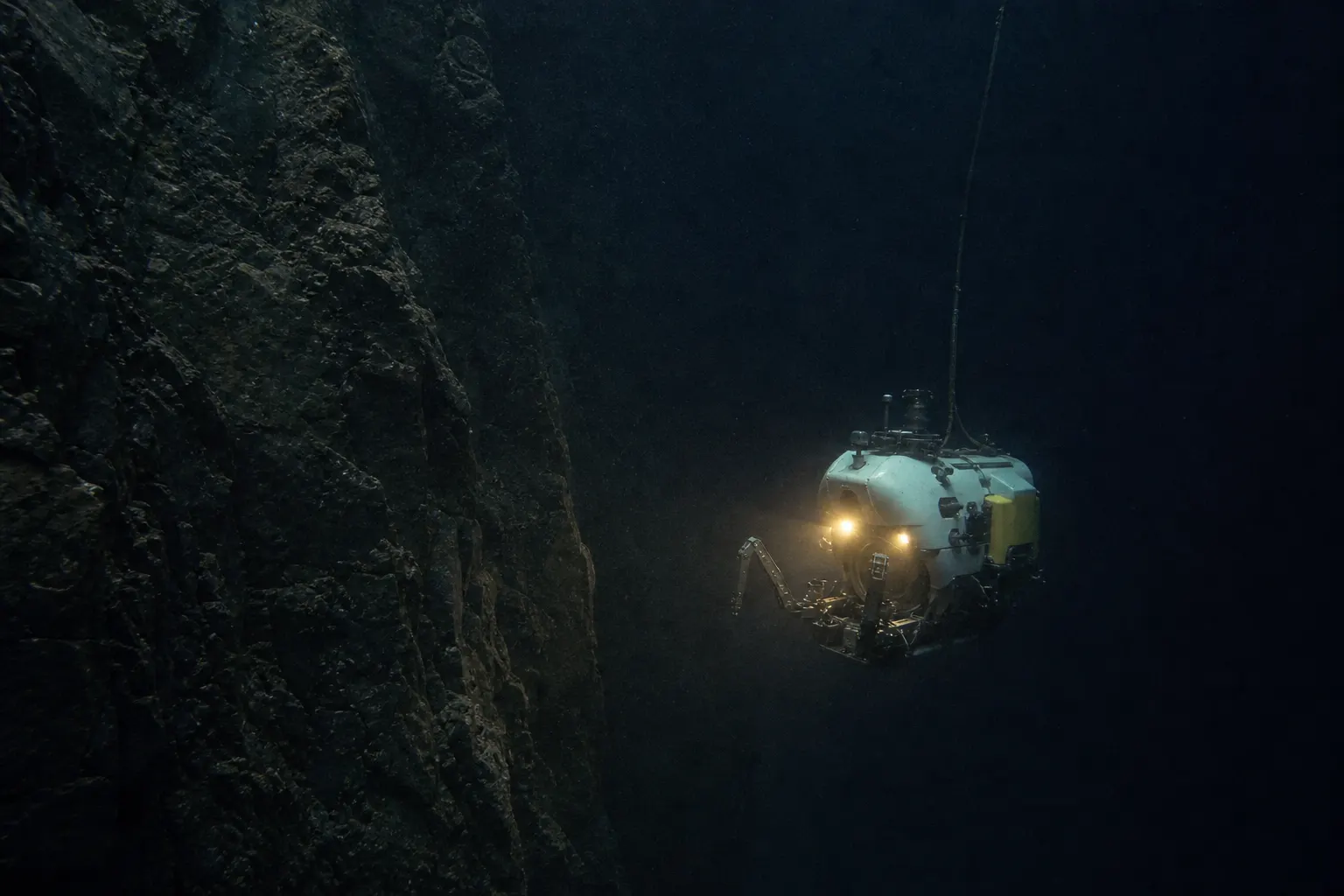 Illustrative deep-sea research submersible descending beside a rock wall.